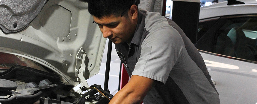 Red classic car parked in front of a sign, two trucks in the background.