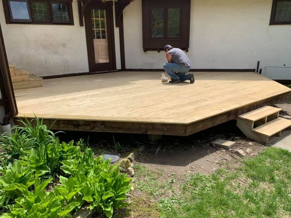 A man is kneeling on a wooden deck in front of a house.