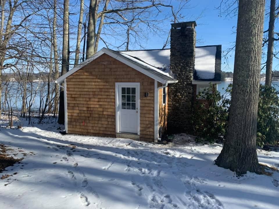 A small house with a chimney is surrounded by snow and trees.