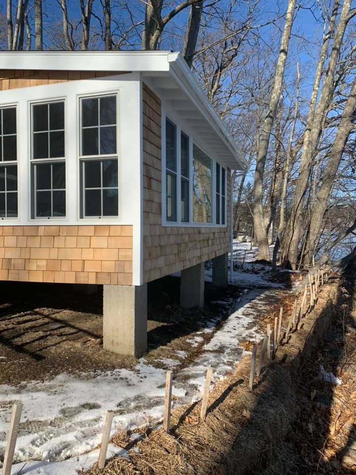 A house with a lot of windows is surrounded by snow and trees