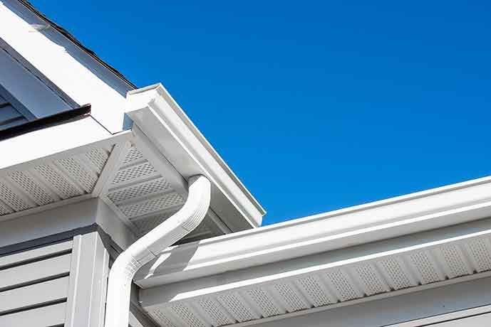 A white gutter on the side of a house with a blue sky in the background.