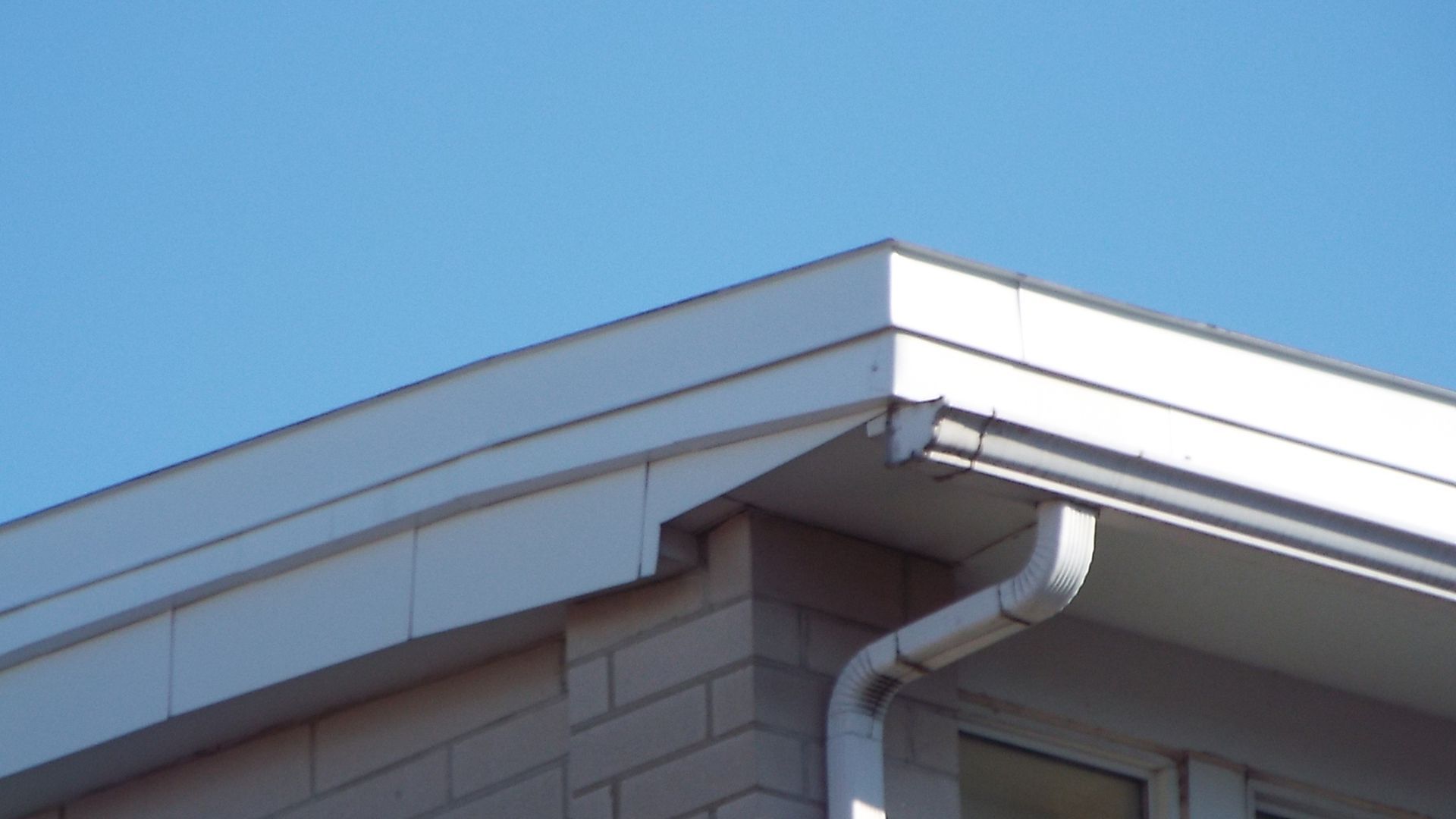 The roof of a house with a white gutter and a blue sky in the background