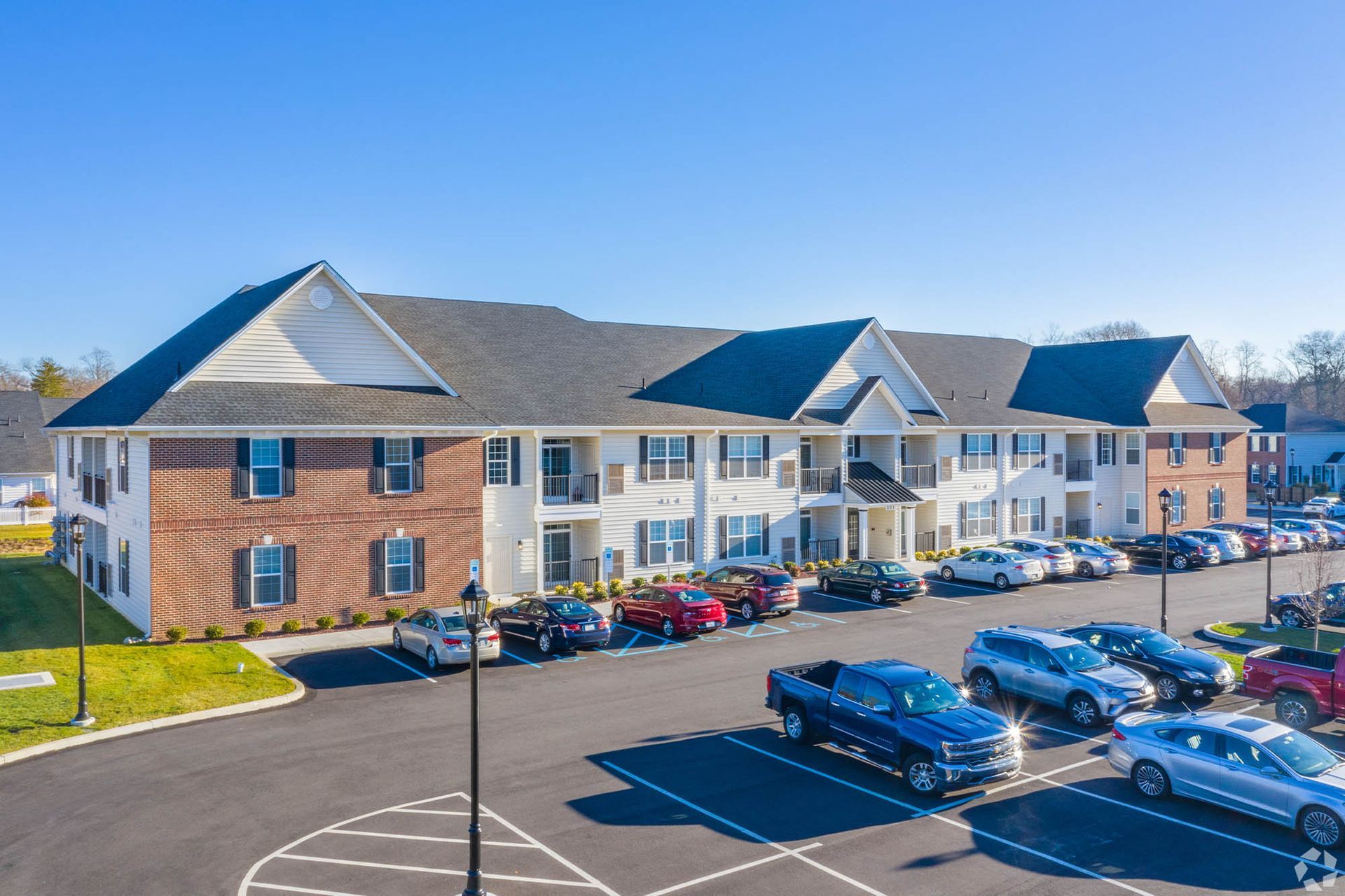 Exterior view of a multi-building apartment community with a large parking lot and cars at The Residences at St. Joseph's Court in Levittown, PA.