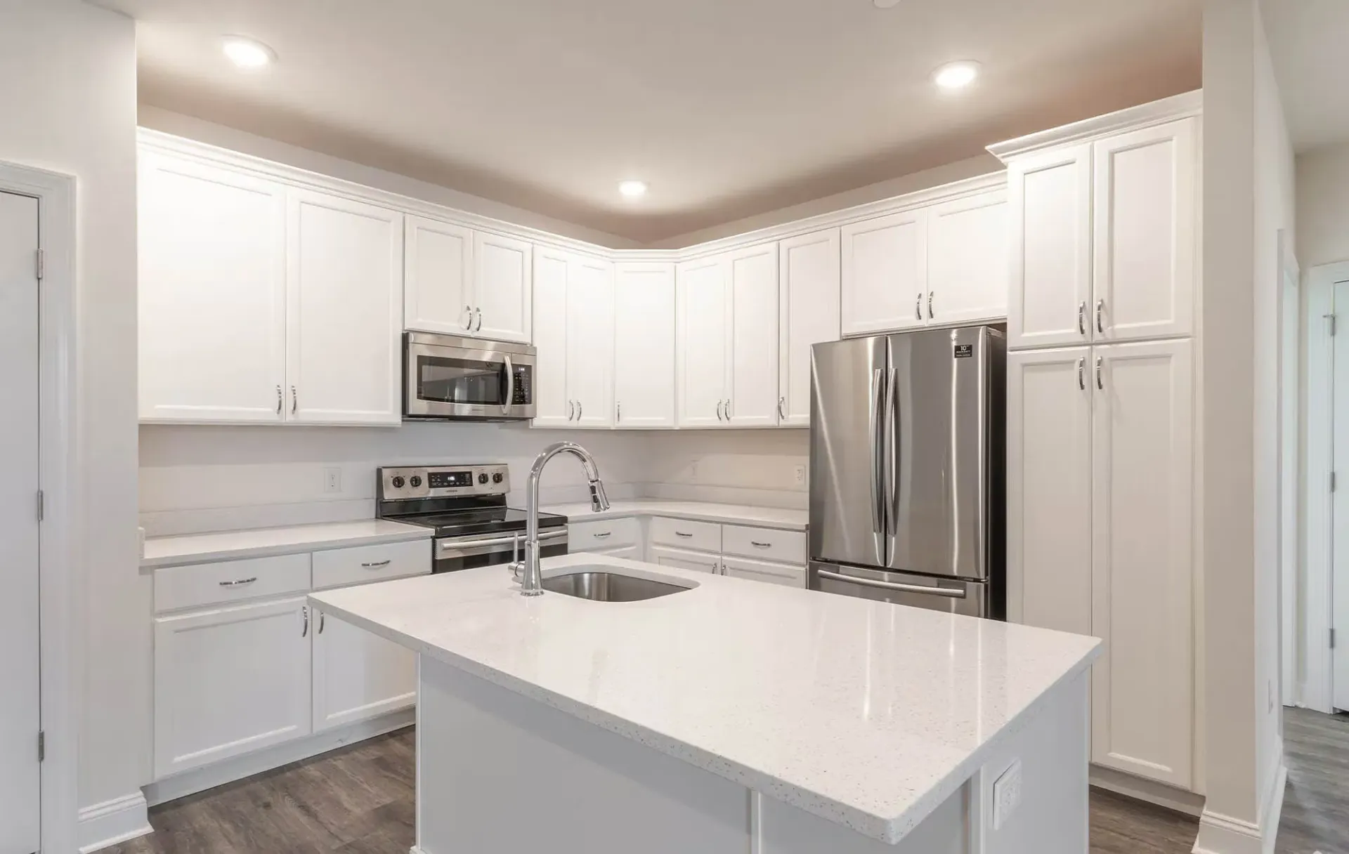 Bright white kitchen with an island, stainless steel refrigerator and microwave, and ample cabinets at The Residences at St. Joseph's Court in Levittown, PA.