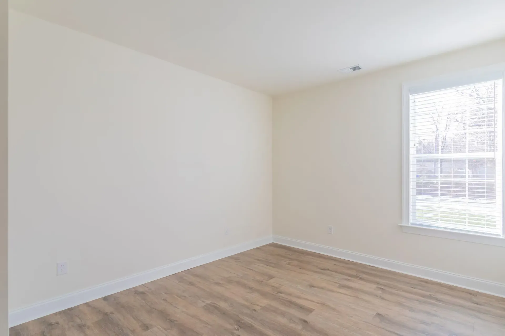 Empty beige bedroom with a large window and wood-look flooring at The Residences at St. Joseph's Court in Levittown, PA.