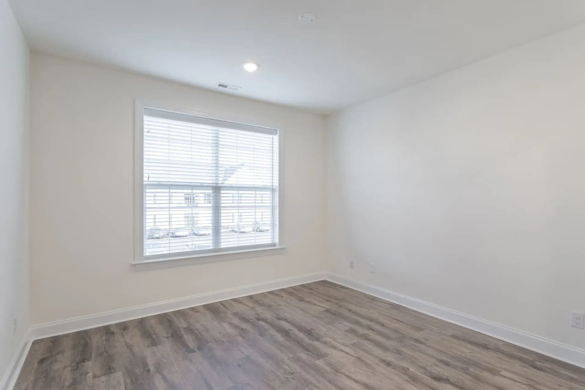 Empty bedroom with a large window, white walls, and light wood-look flooring at The Residences at St. Joseph's Court in Levittown, PA.
