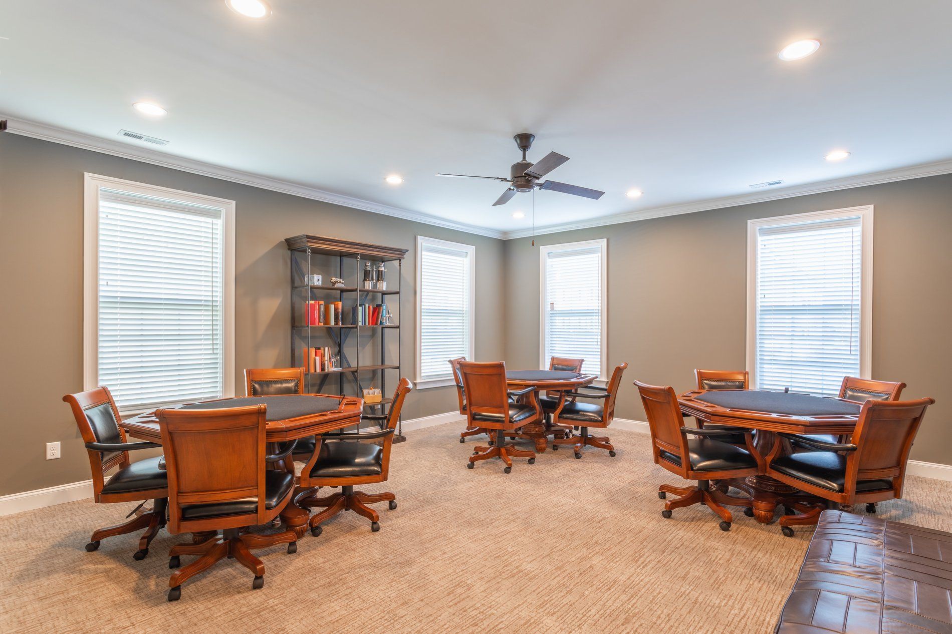 Interior community lounge with round tables, upholstered chairs, a ceiling fan, and large windows at The Residences at St. Joseph's Court in Levittown, PA.