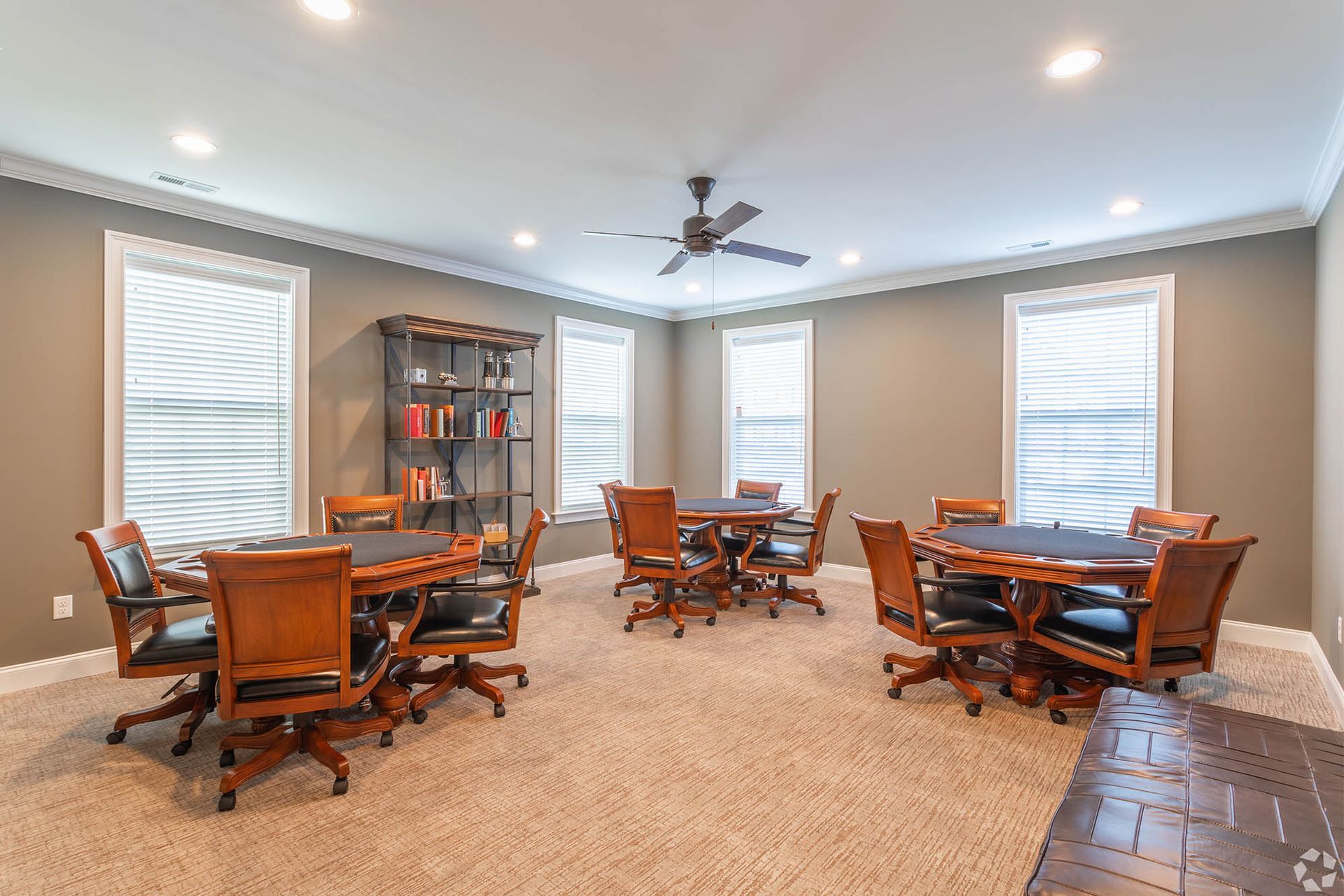 Interior of a community lounge with round tables, wooden chairs, and a bookshelf at The Residences at St. Joseph's Court in Levittown, PA.