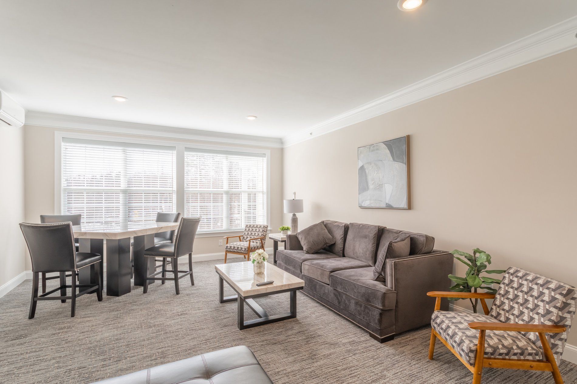Living room with sofa, table, chairs, and large windows. Neutral color scheme.