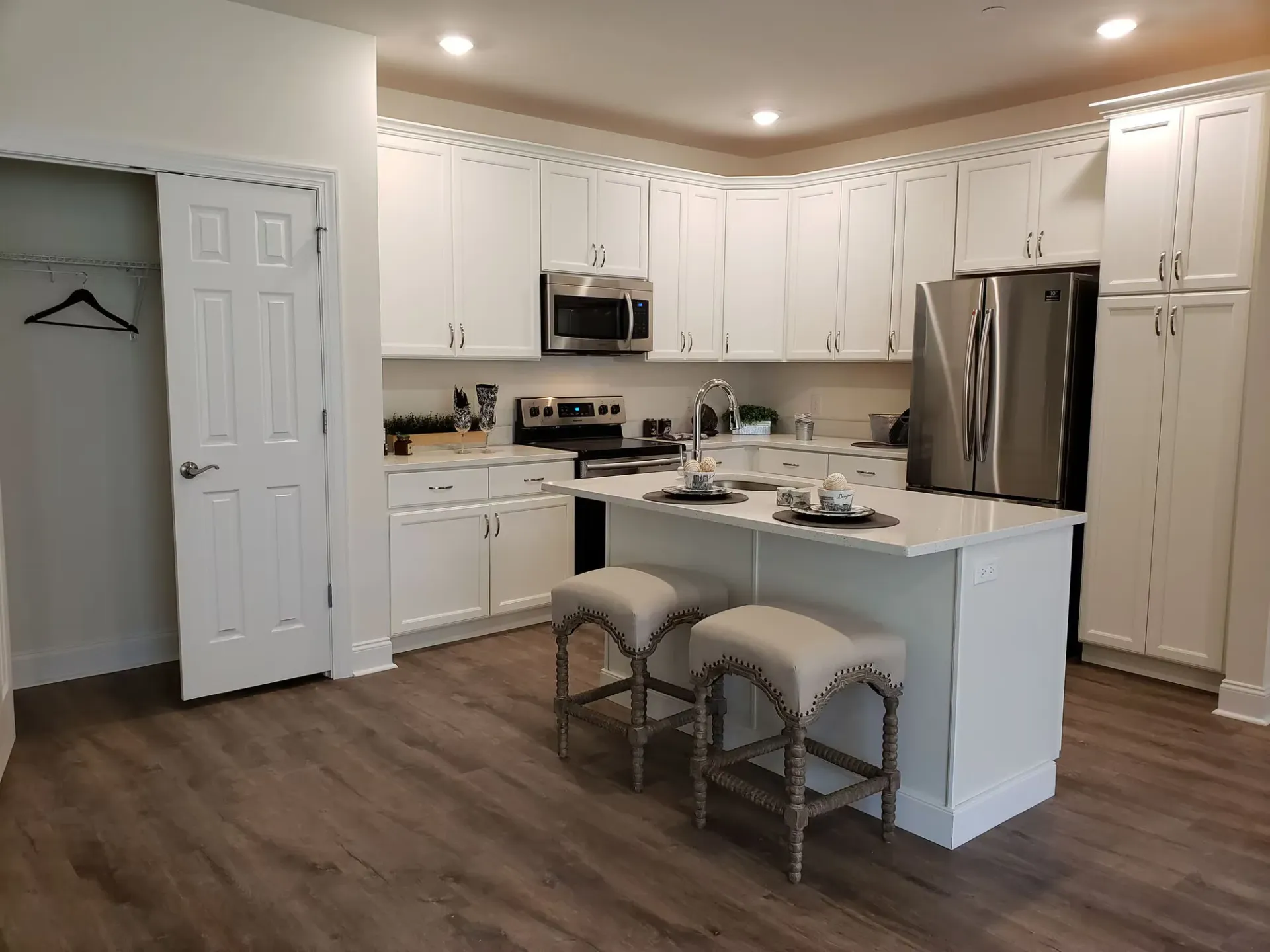 White kitchen with stainless steel refrigerator, island, and two upholstered bar stools at The Residences at St. Joseph's Court in Levittown, PA.