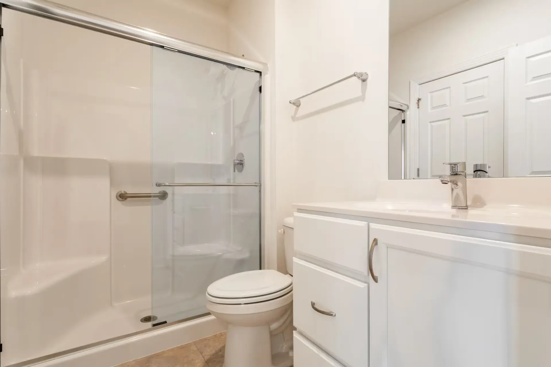 Bright bathroom with a glass sliding shower, white toilet, and white vanity at The Residences at St. Joseph's Court in Levittown, PA.