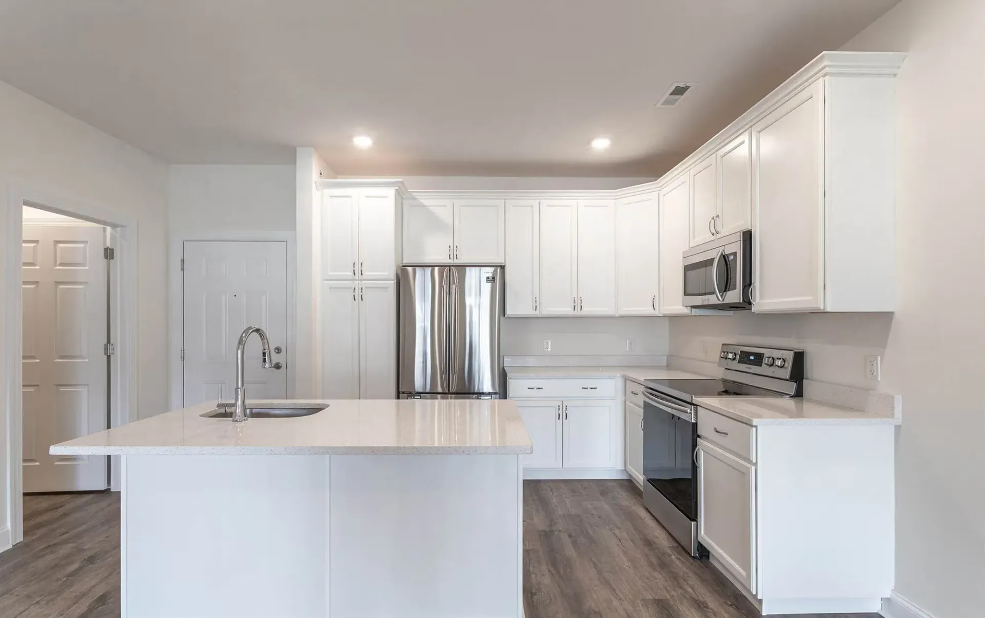 Open-concept kitchen with white cabinets, island, and stainless steel appliances at The Residences at St. Joseph's Court in Levittown, PA.