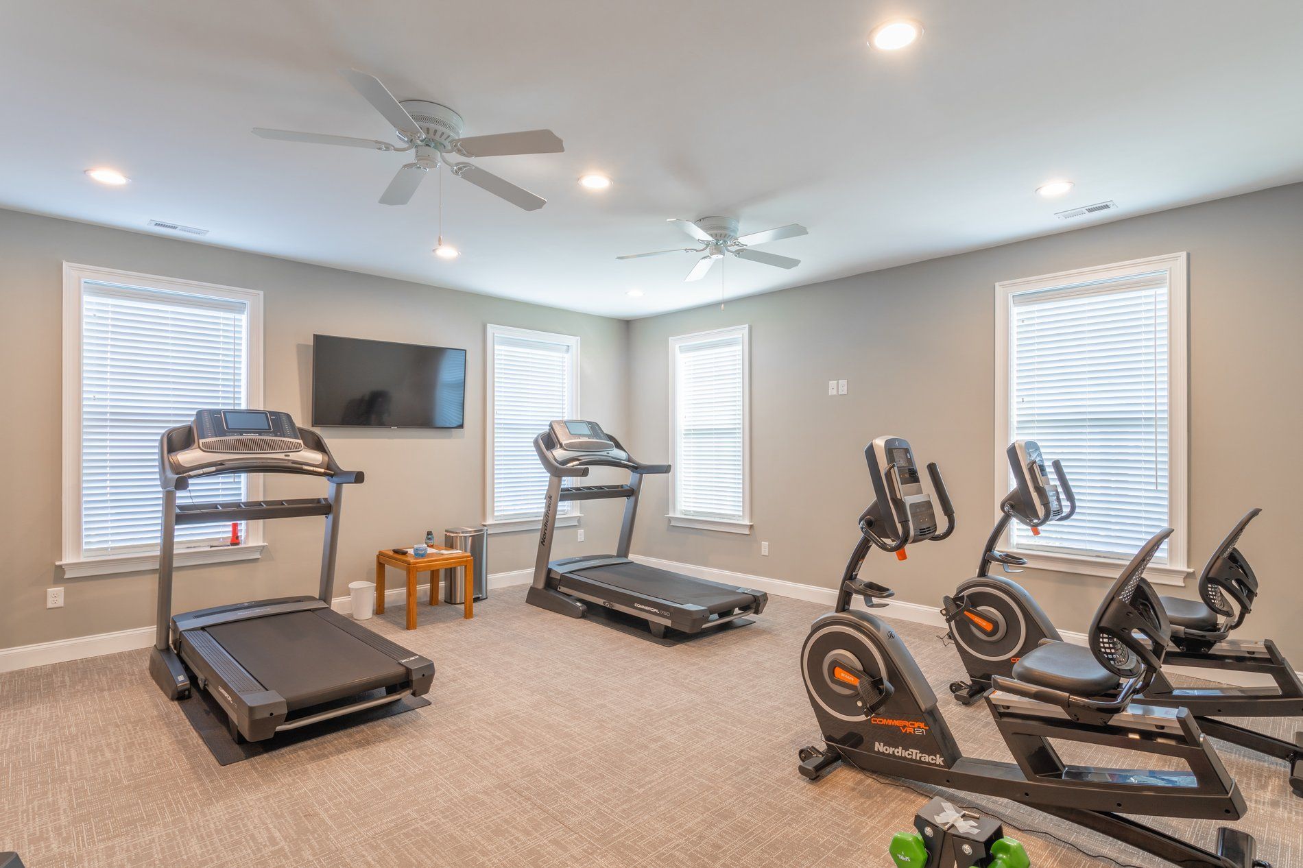 Community gym featuring treadmills, stationary bikes, a wall-mounted TV, and large windows at The Residences at St. Joseph's Court in Levittown, PA.