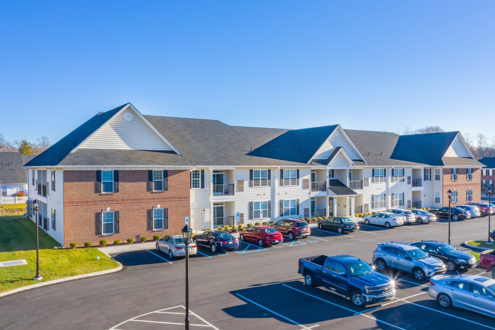 Exterior view of a multi-building apartment complex with a parking lot in front at The Residences at St. Joseph's Court in Levittown, PA.
