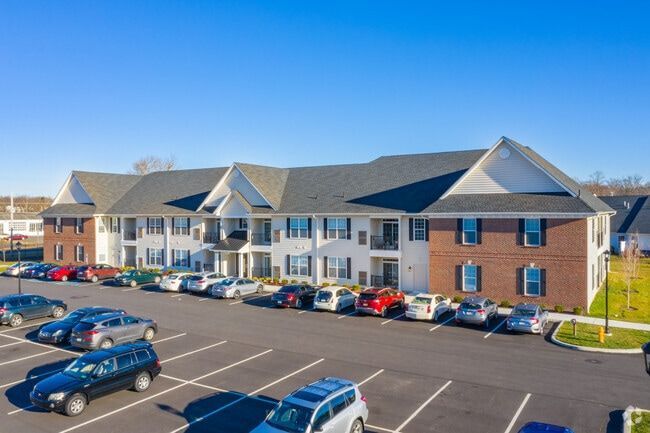 Apartment complex with brick and white siding, ample parking, and a blue sky.