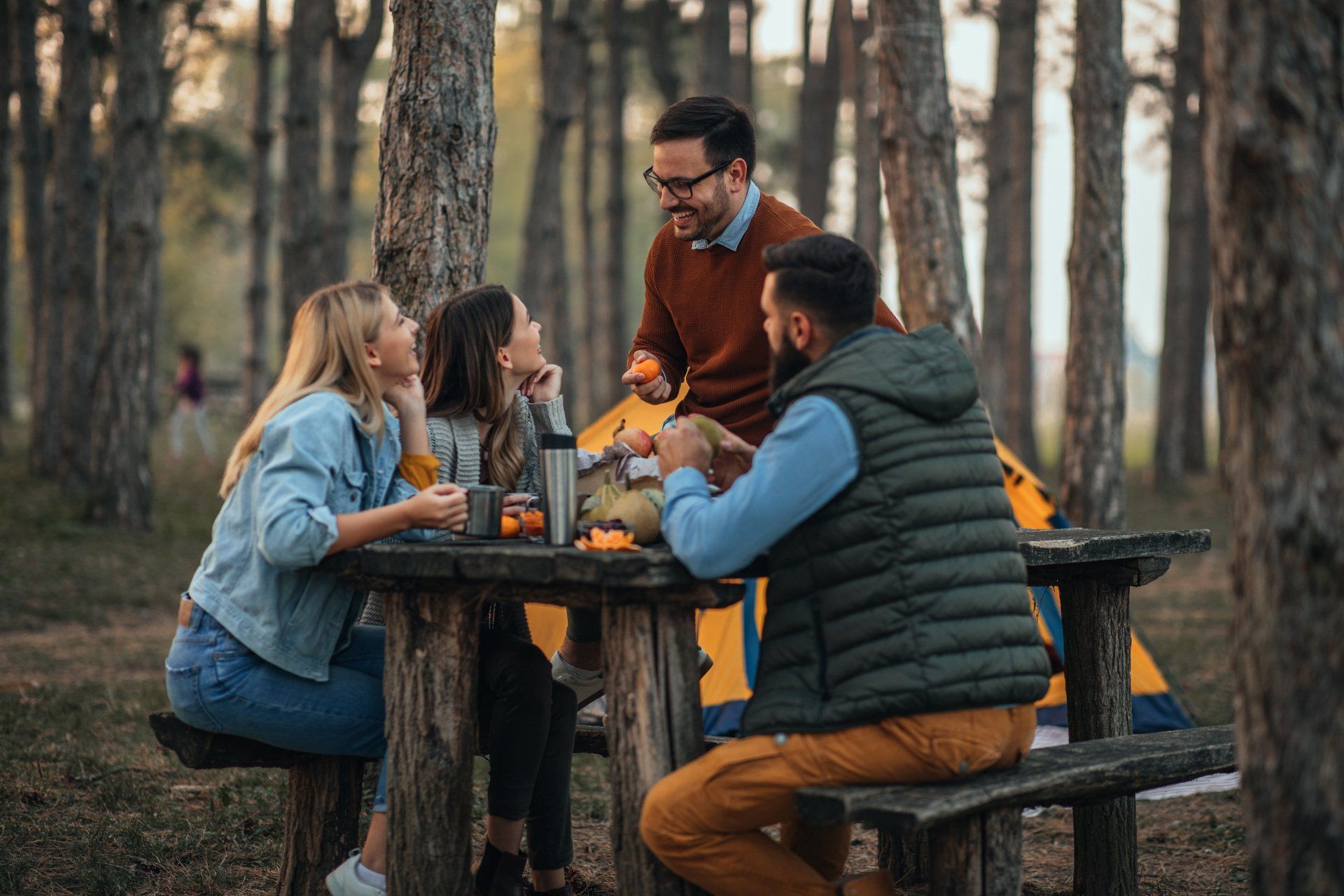A group of people are sitting at a picnic table in the woods.