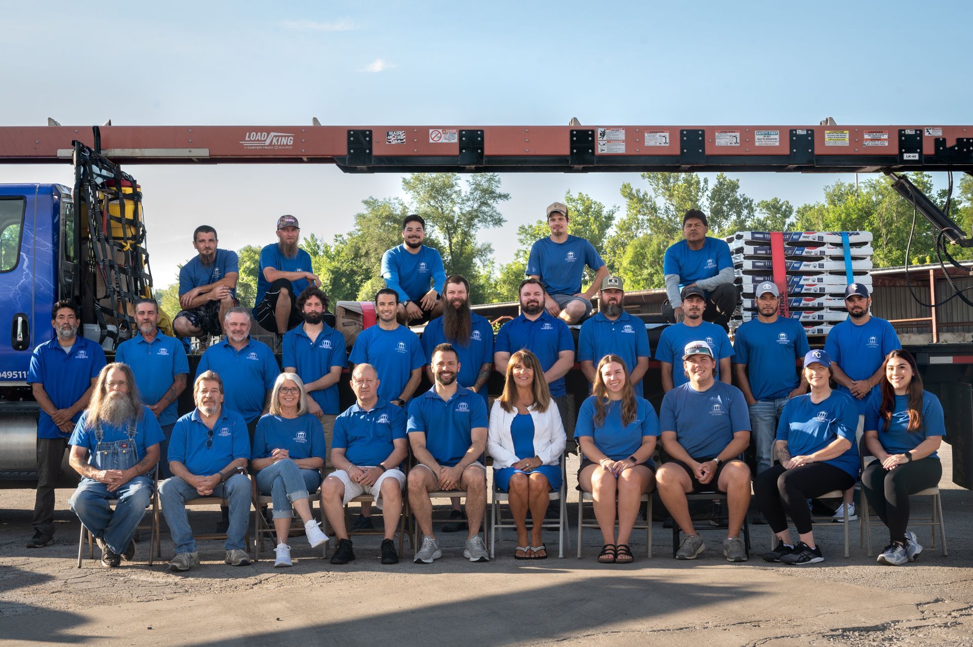 Group photo of diverse people in blue shirts, posing in front of a truck with a crane.