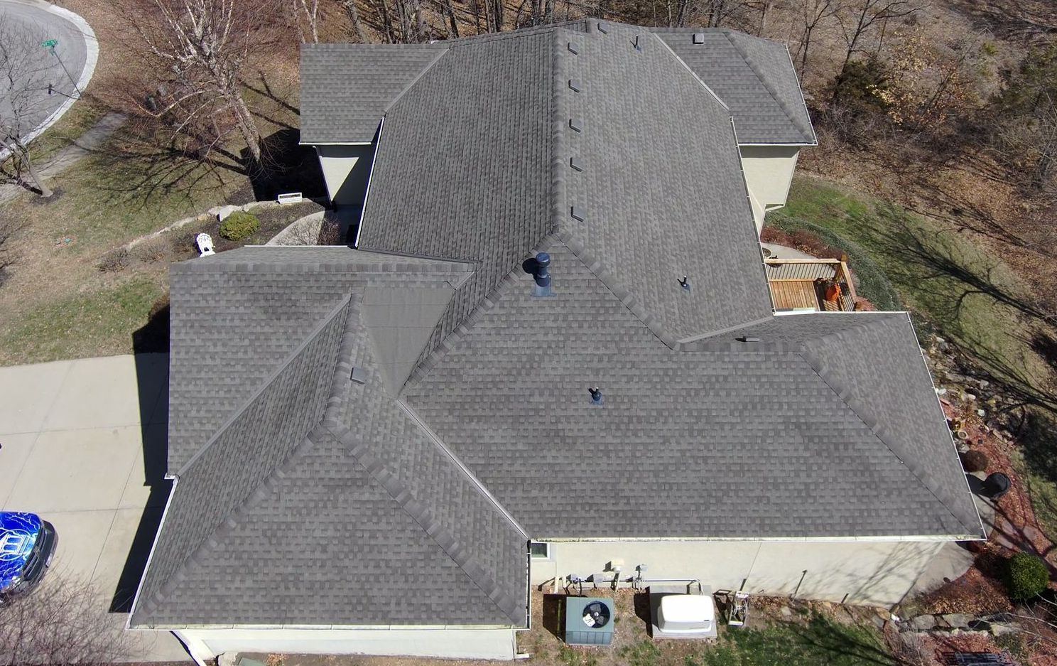 Overhead view of a house with a gray roof and surrounding greenery, trees, and driveway.