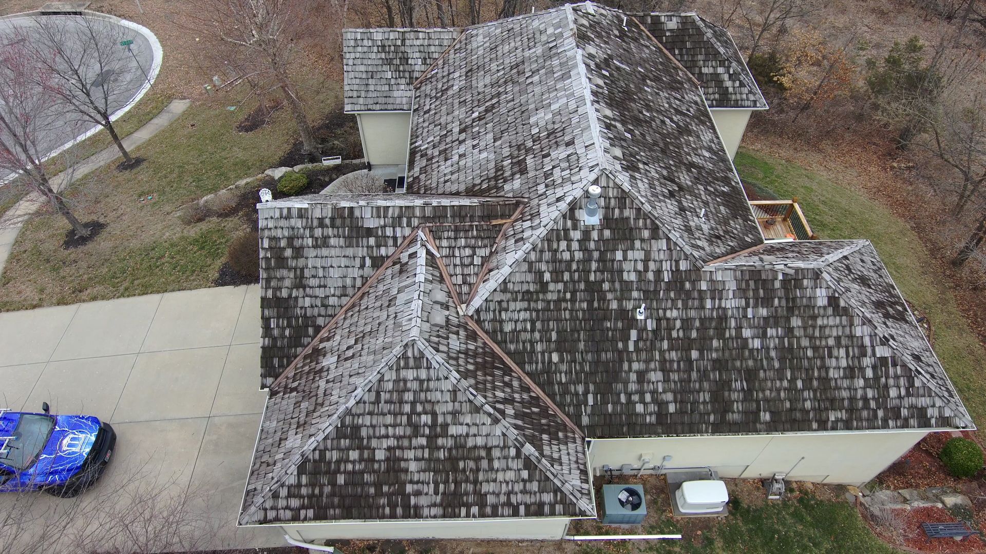 Overhead view of a home with a weathered, mossy wood shake roof, a driveway, and a blue car.