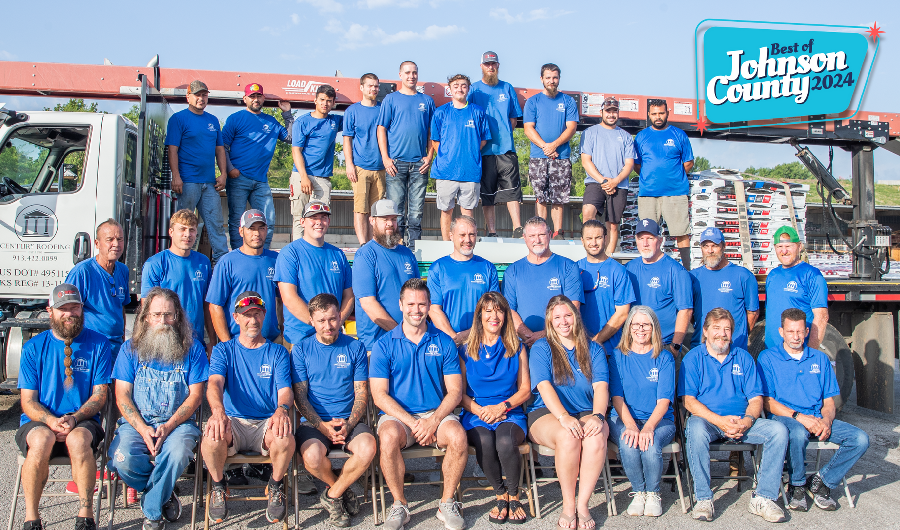 Group of people in blue shirts, posing with a truck,