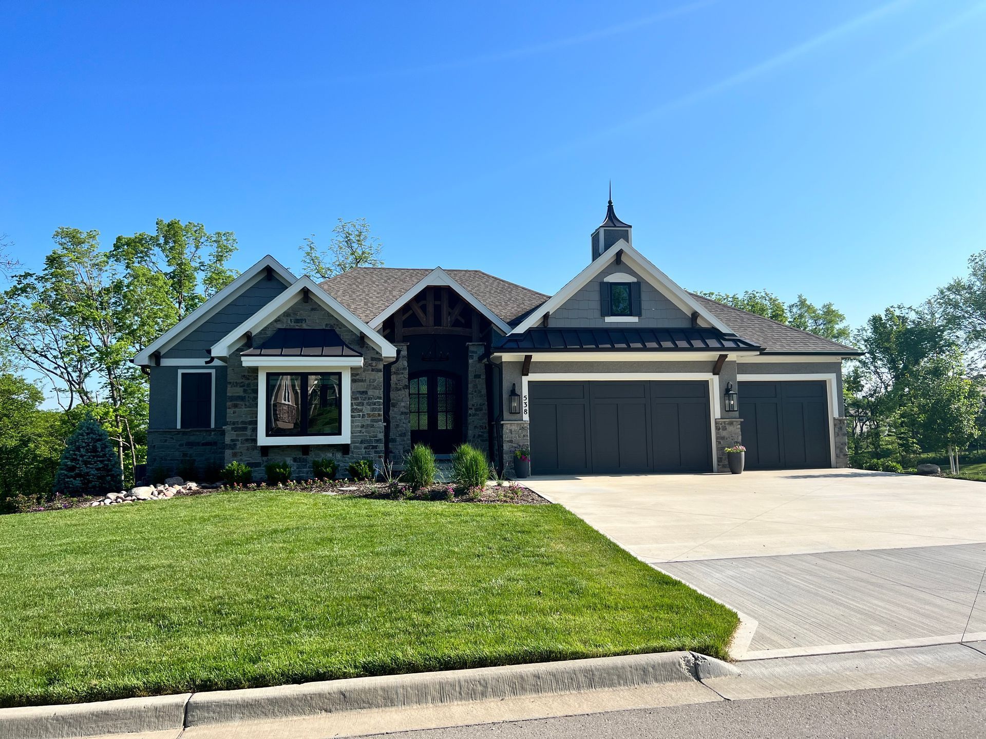 Modern home with stone accents, grey siding, and a green lawn on a sunny day.
