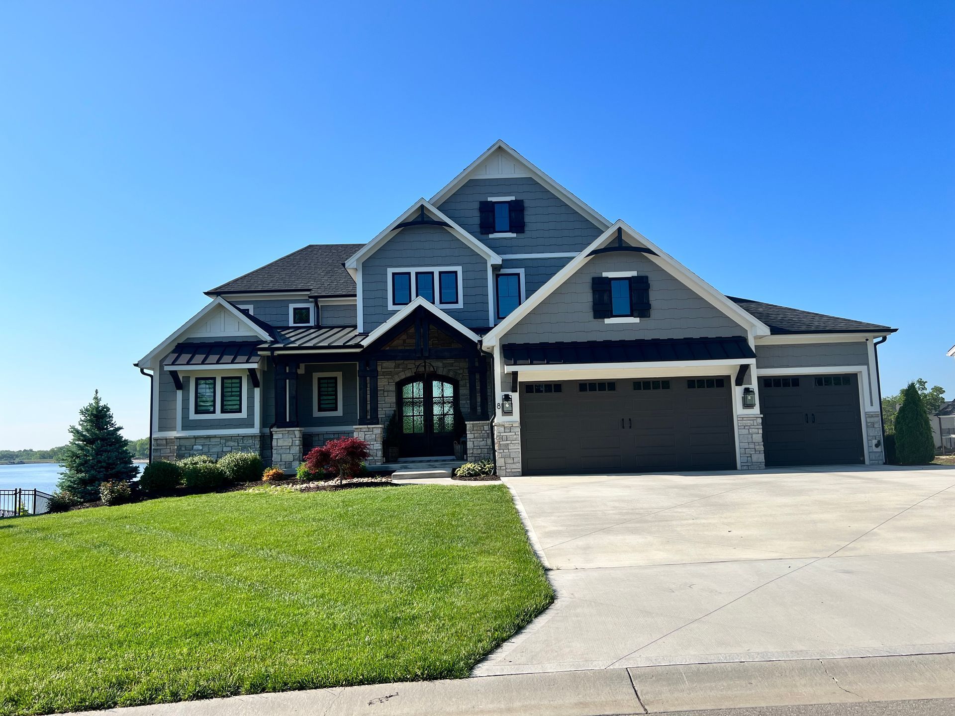 Two-story blue-gray house with a three-car garage and green lawn on a sunny day.