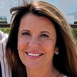 Woman with brown hair smiling outdoors, wearing earrings.