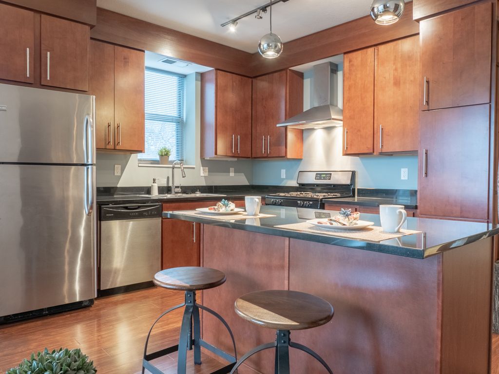 Modern kitchen with stainless steel appliances, wood cabinets, and a breakfast island with stools.