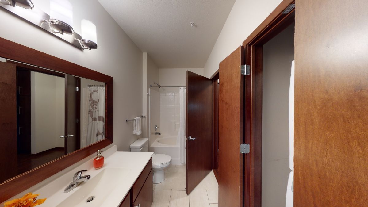 Bathroom with double sink, large mirror, shower, and open wooden door to the hallway