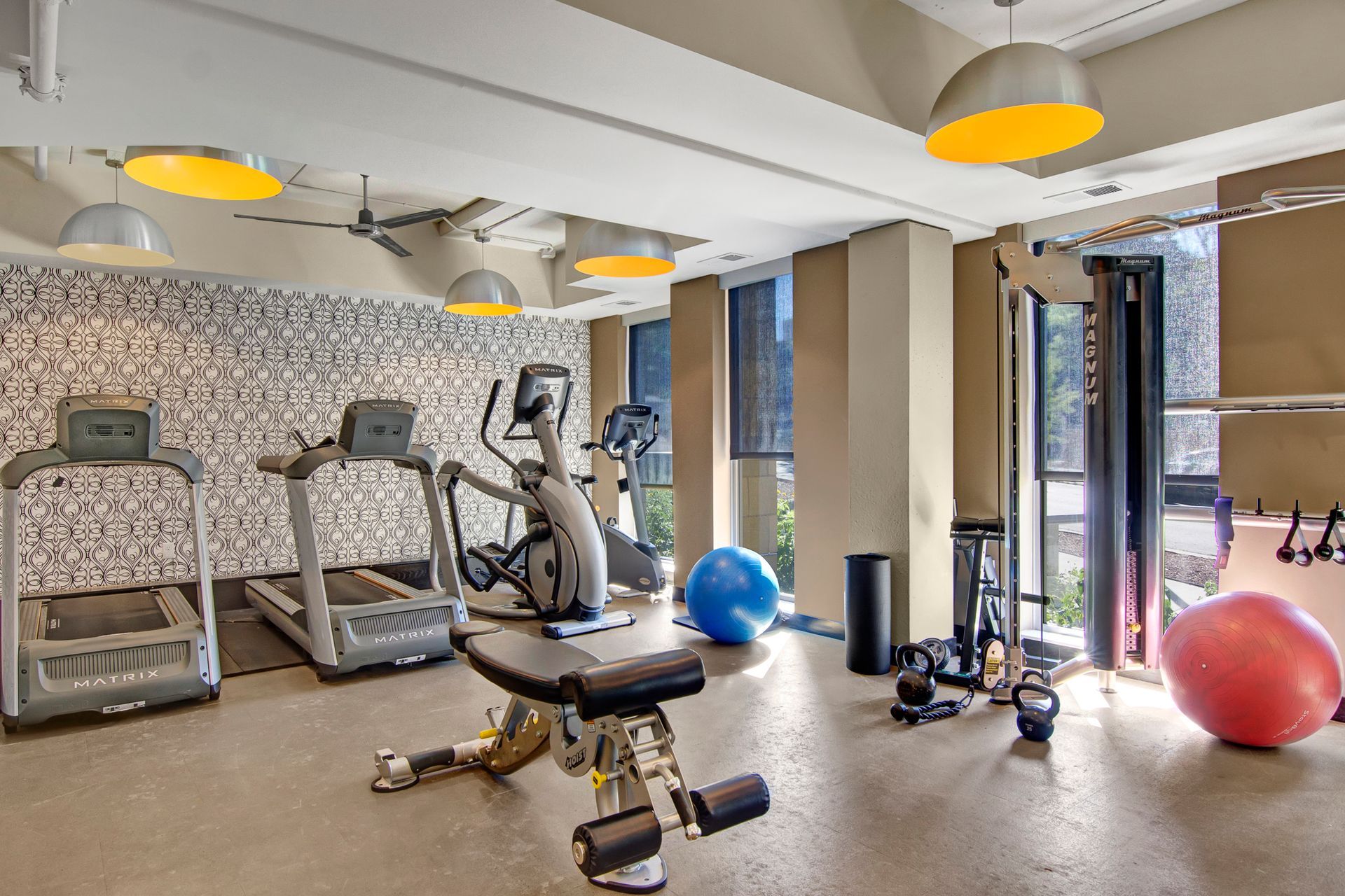 Gym with treadmills, elliptical, weights, and colorful exercise balls in a bright room.