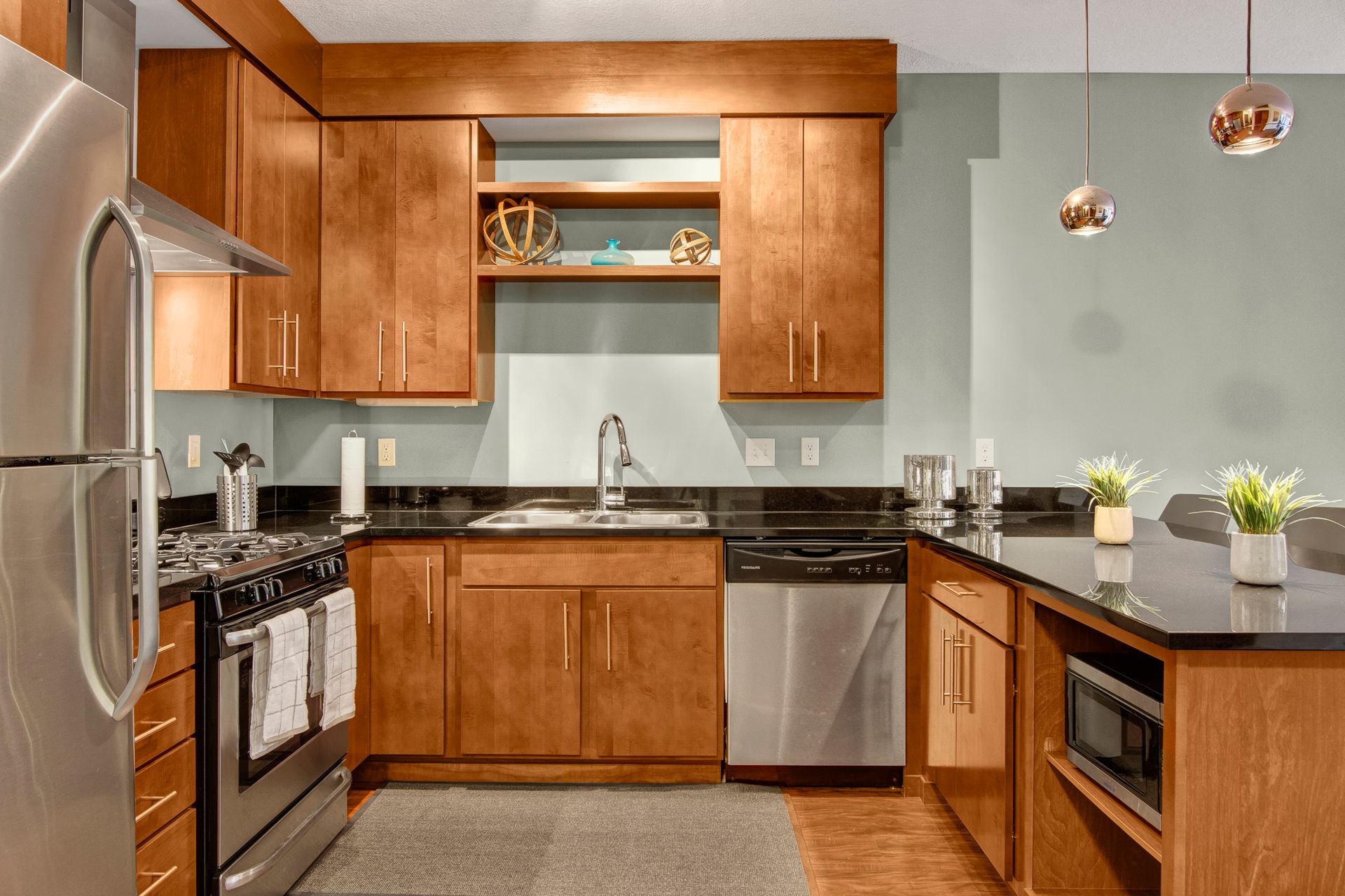 Modern kitchen with wood cabinets, black countertops, stainless appliances, and pendant lights