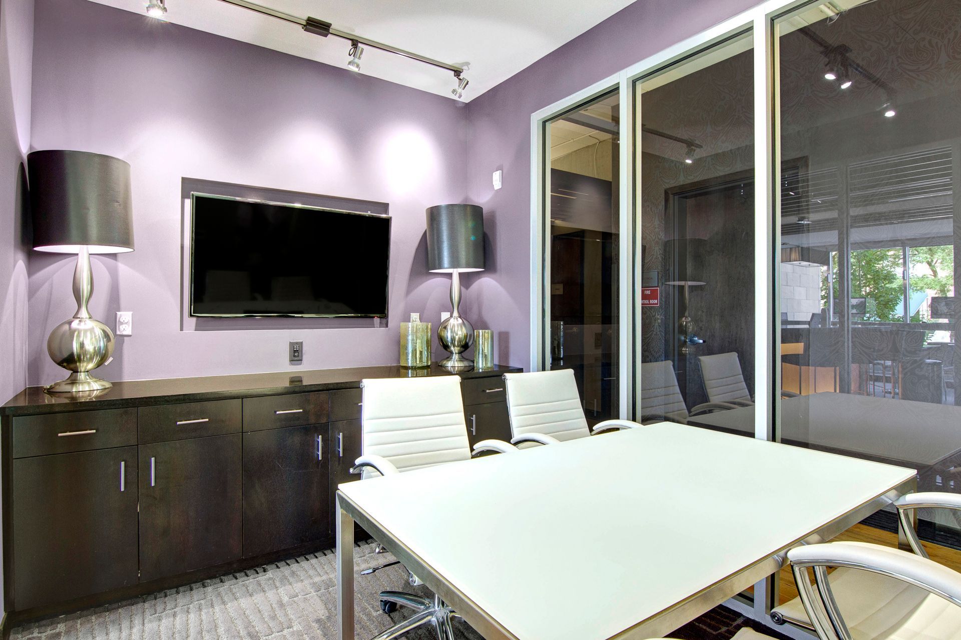 Modern conference room with white table, black cabinets, wall-mounted TV, and glass partition.
