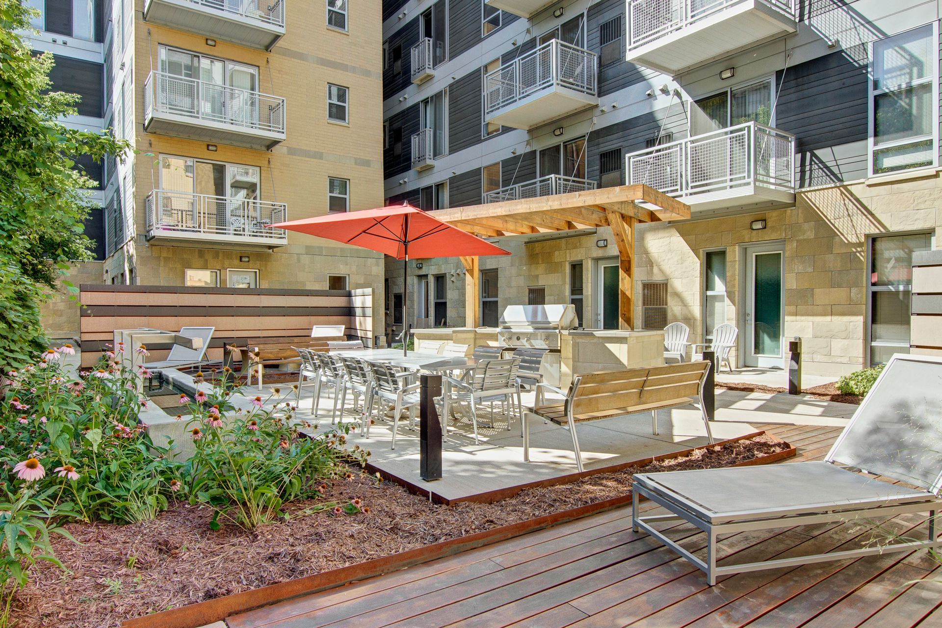 Outdoor apartment courtyard with patio seating, red umbrellas, and lounge chairs surrounded by buildings