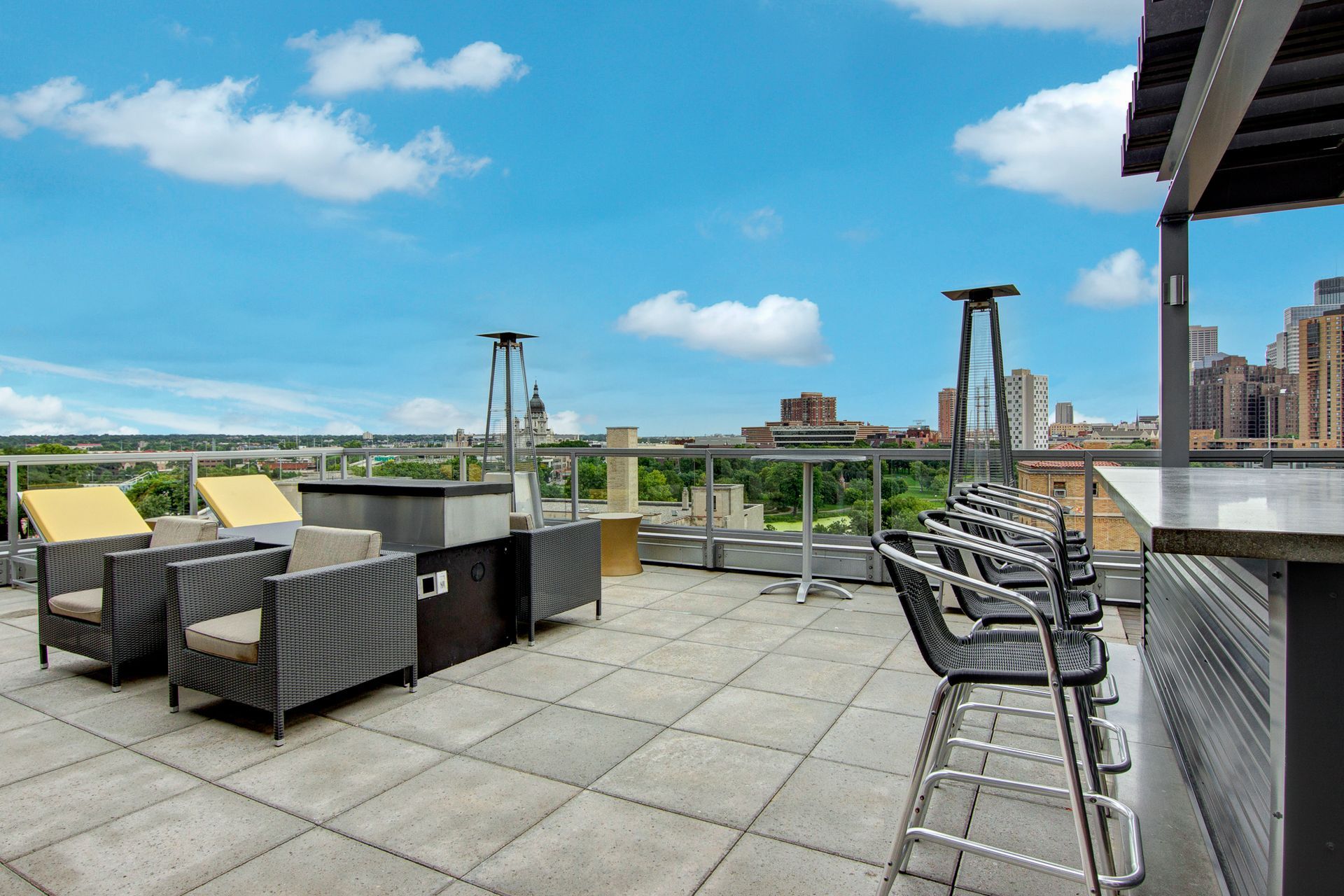 Rooftop patio with wicker seating, bar stools, and city skyline under a blue sky
