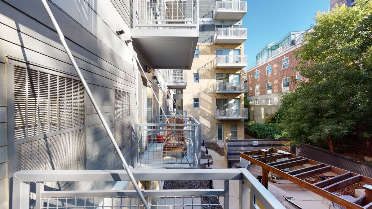 Outdoor apartment walkway with metal stairs, balconies, and industrial railings in a narrow courtyard.