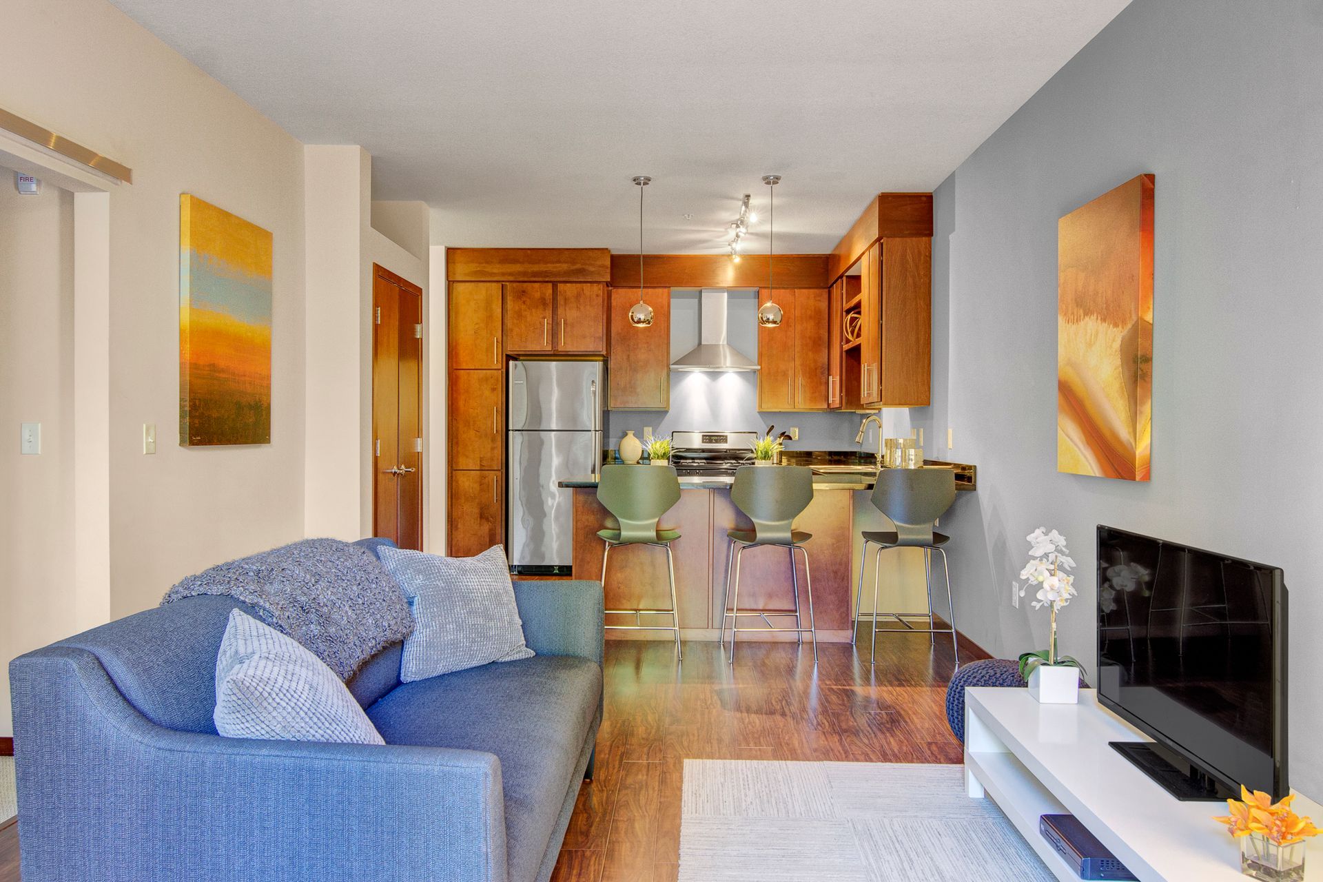 Cozy living room and kitchen with blue sofa, breakfast bar stools, and wall art in warm wood tones