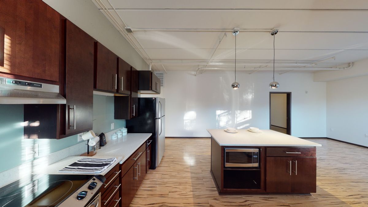 Empty modern kitchen with dark cabinets, white countertops, and a large island in a bright open room