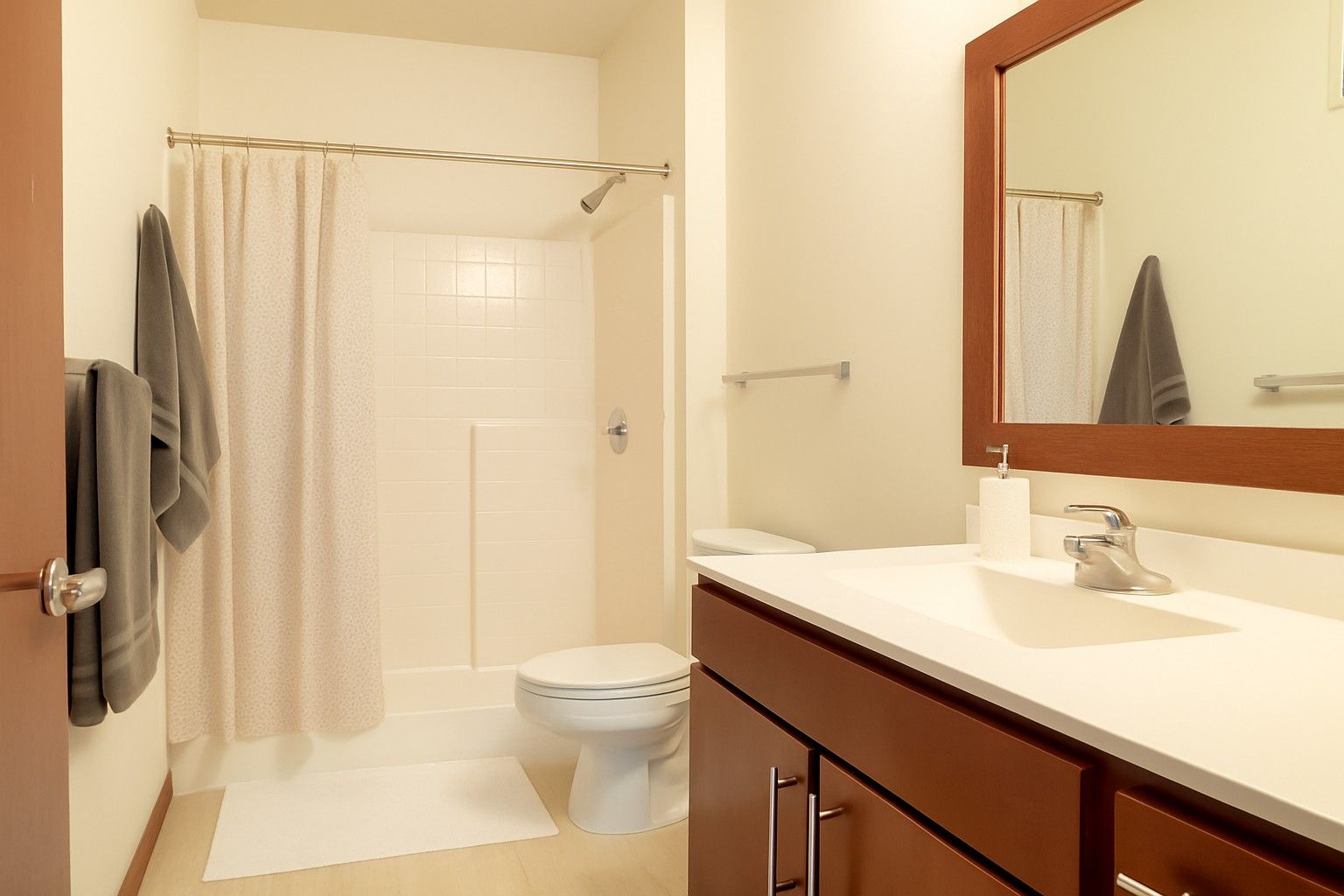 Bright bathroom with a white shower curtain, toilet, and dark wood vanity with mirror.