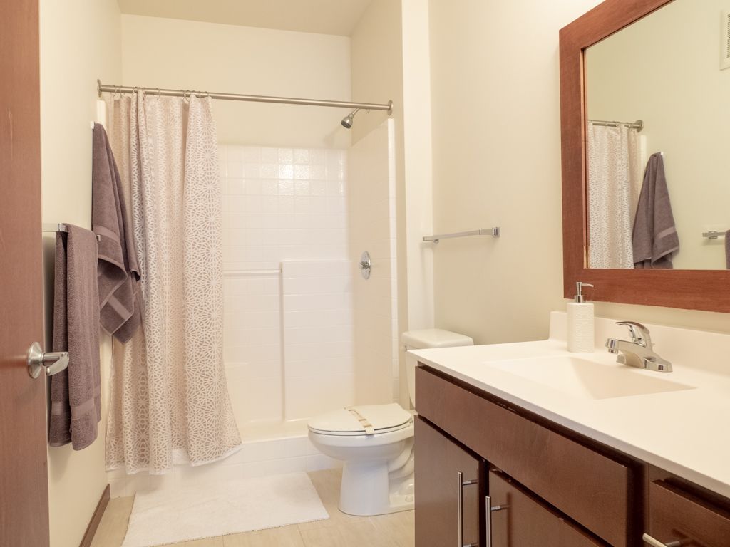 A bathroom with a toilet , sink , mirror and shower curtain.