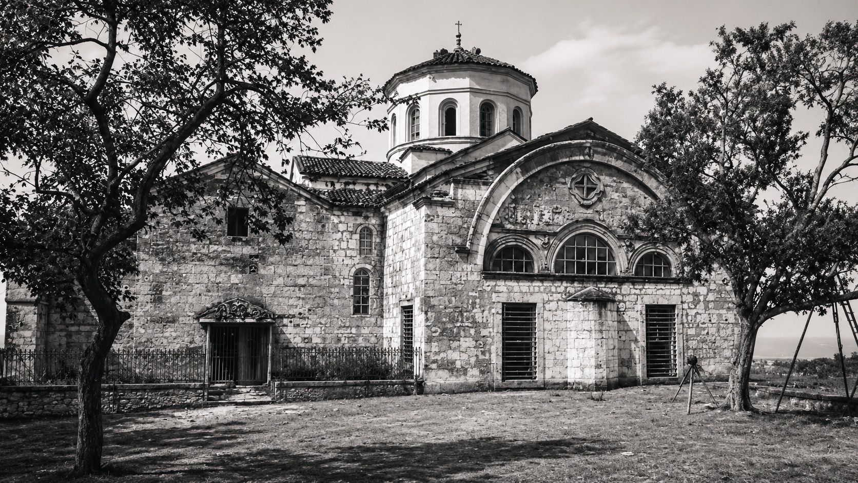 A historic stone church with a central dome, arched windows, and weathered exterior walls, surrounded by trees.