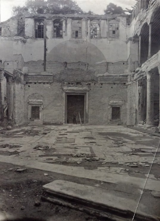 A black and white, eye-level view of the interior ruins of a historic stone building with a central arched doorway.