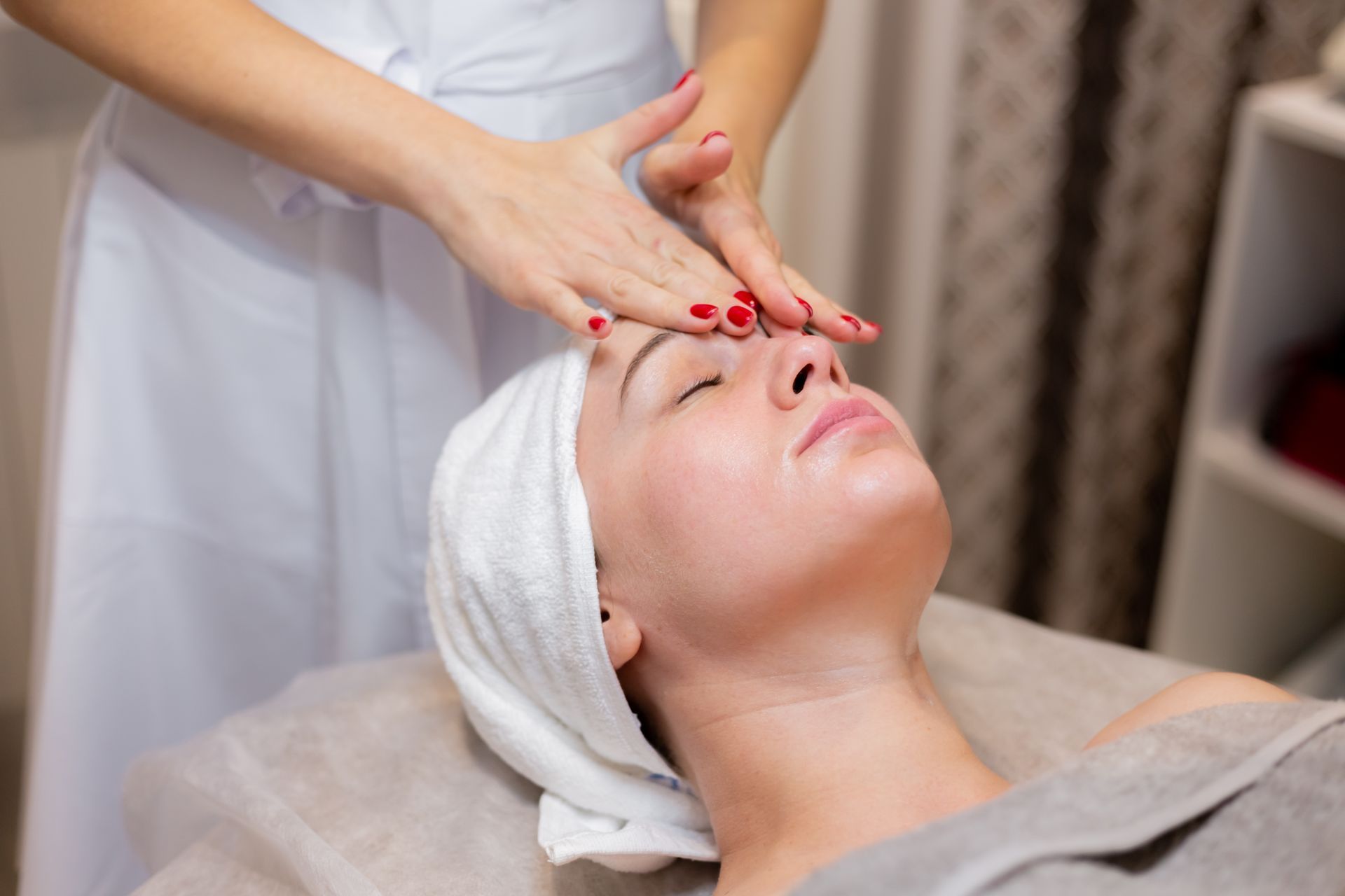A woman with a towel wrapped around her head is getting a facial massage at a spa.