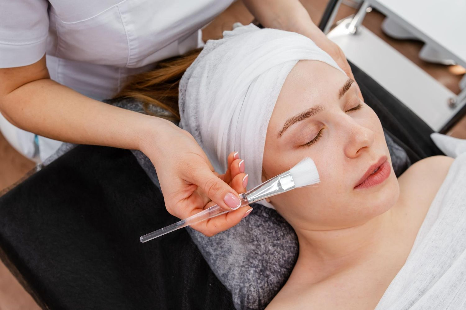 A person receiving a facial treatment; technician applying a mask with a brush.