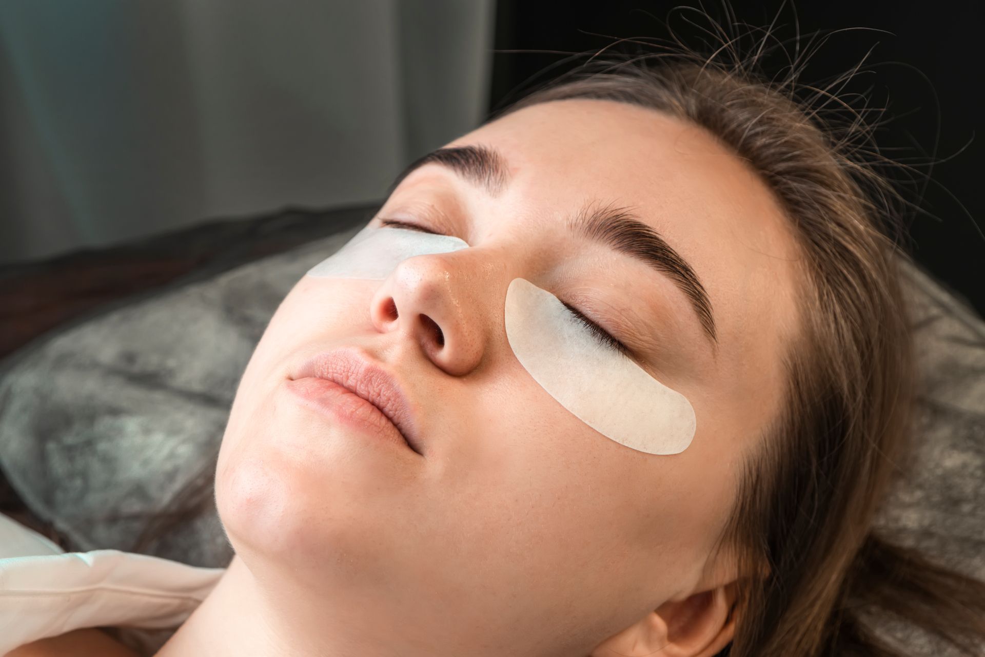 A woman is laying on a bed with eye patches on her eyes.