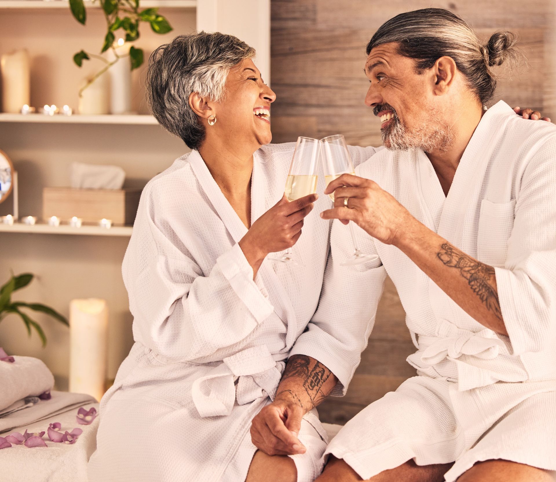 Couple in white robes toasting champagne, spa setting, smiling.