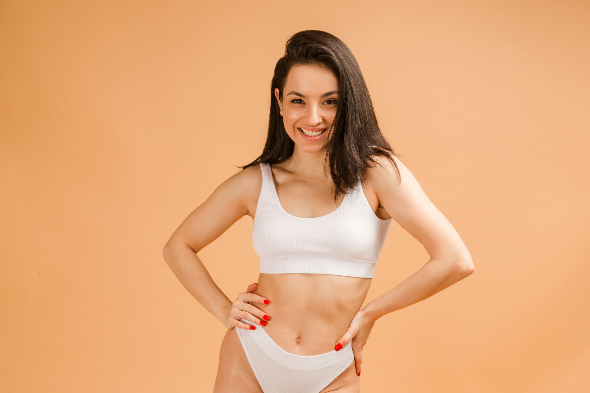 A woman in white underwear is standing with her hands on her hips and smiling.