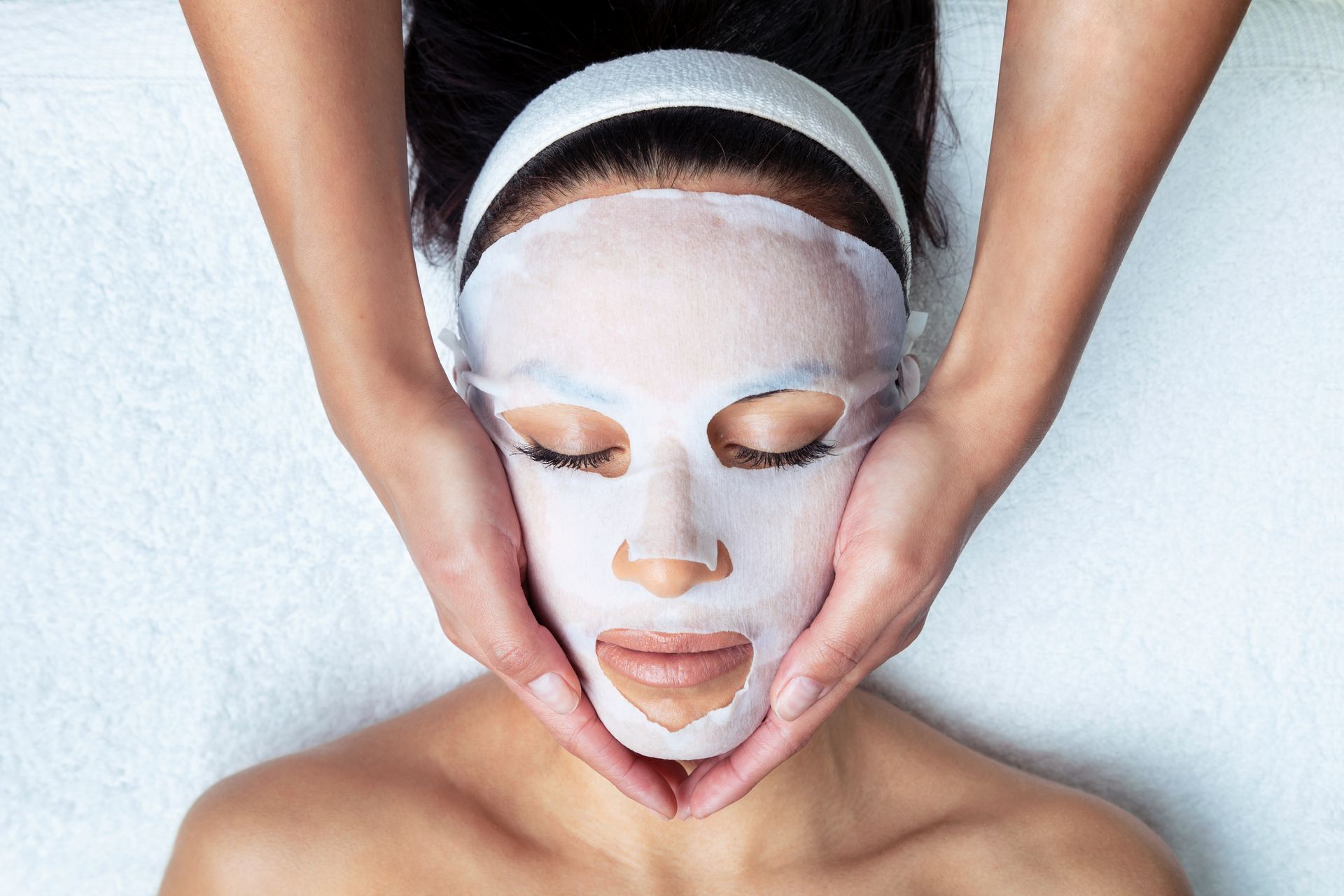 A woman is getting a facial treatment with a sheet mask on her face.