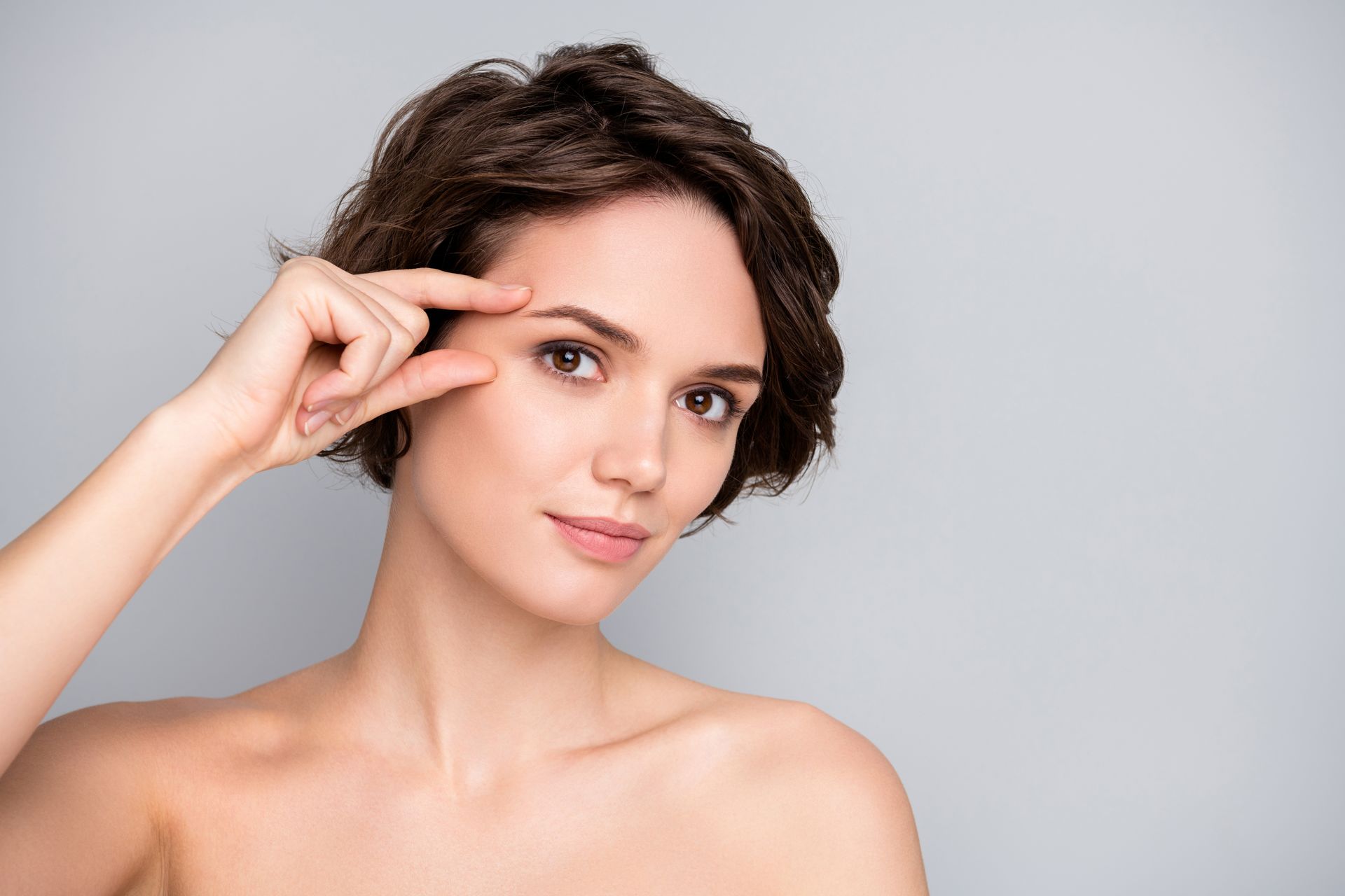 A woman is pointing at her eye with her finger.