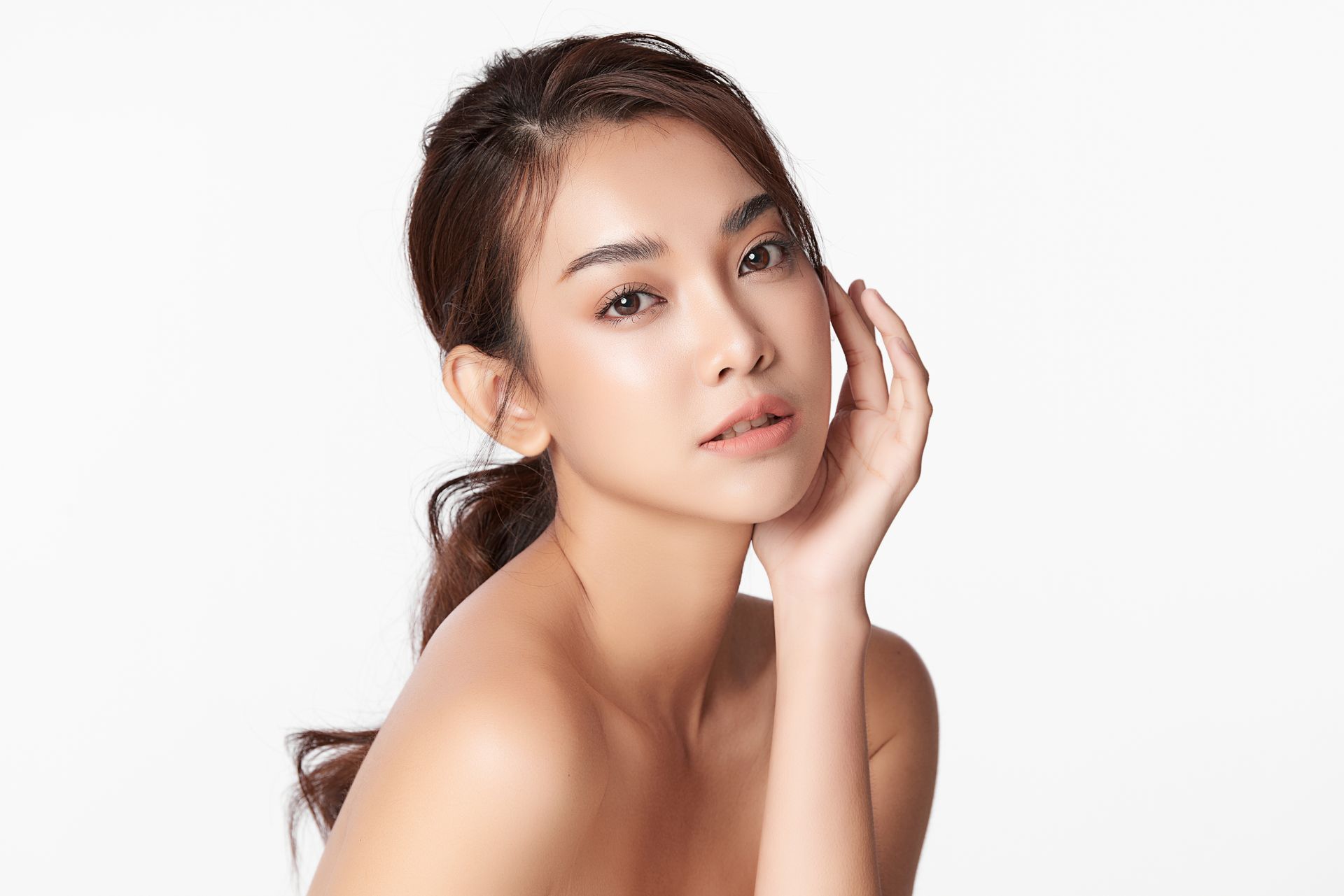 Portrait of a woman with tied-back hair, touching her face against a white background