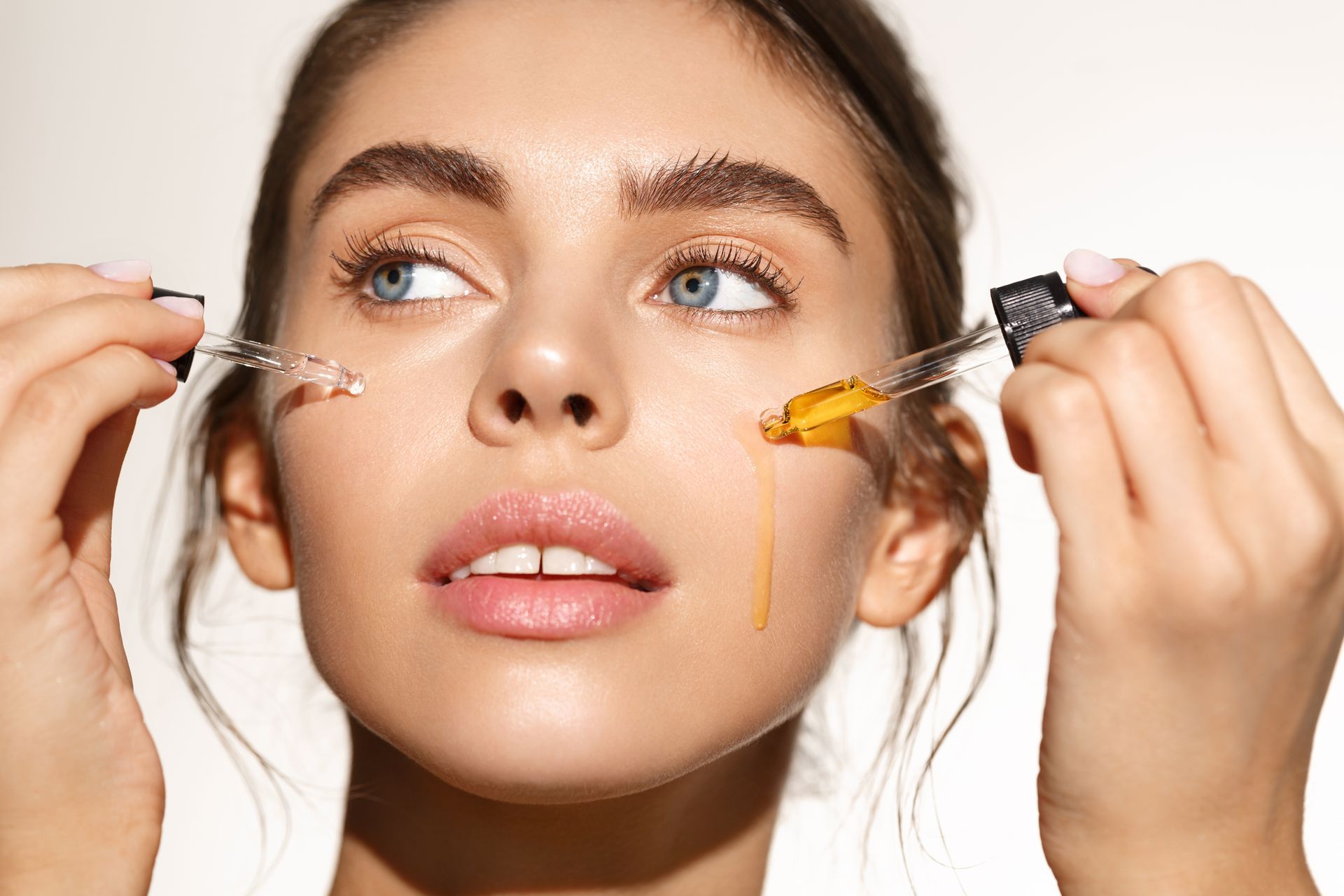 A woman is applying a serum to her face with a pipette.